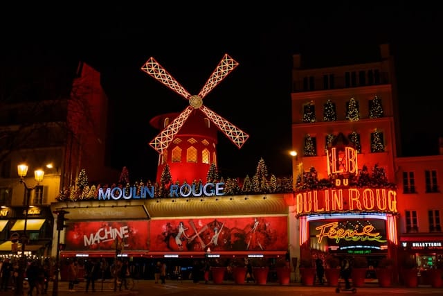 Brightly lit Moulin Rouge with people waiting outside