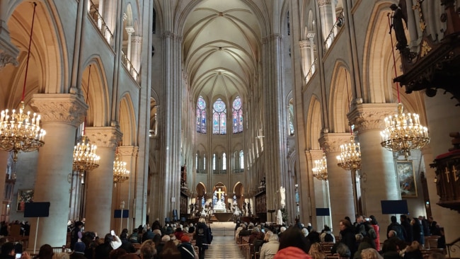 Catholic Mass service underway at Notre Dame Cathedral Paris with congregation seated in nave and priest at altar.
