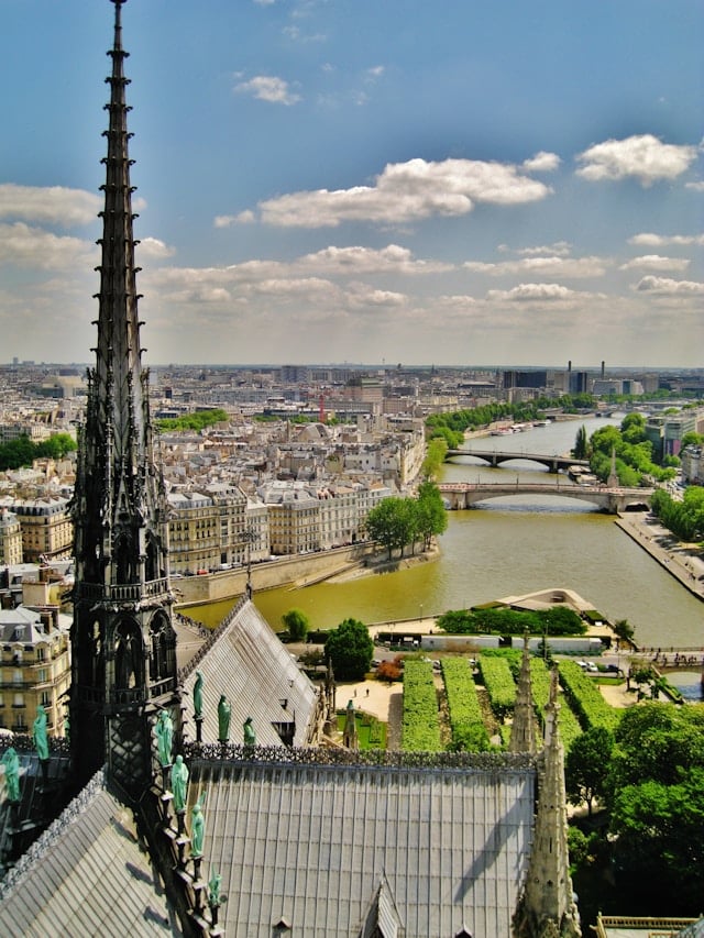 Panoramic view of Paris from Notre Dame Cathedral bell tower showing Seine River, bridges, and Parisian rooftops.