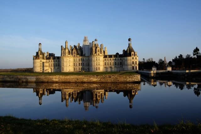 Sunset view of Chambord Castle from the canal showing the full reflection in still water.