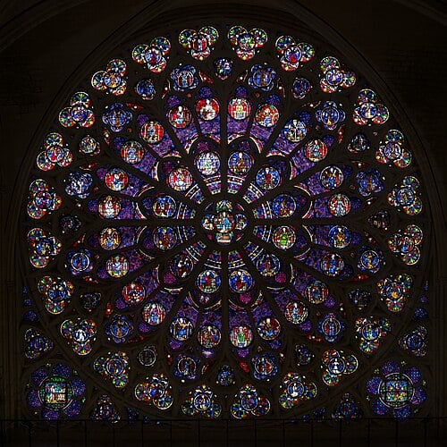 The magnificent south rose window of Notre Dame with its warm red and gold tones depicting Christ surrounded by saints and apostles.