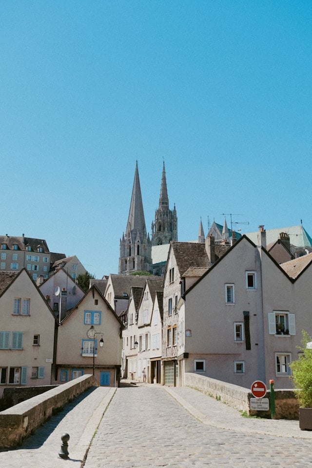 Chartres Cathedral viewed from the medieval lower town along the Eure river, the cathedral's mass rising above half-timbered houses and riverside gardens — the view that rewards visitors who explore beyond the cathedral itself