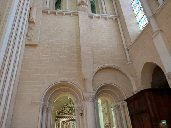 Interior of Chartres Cathedral nave showing restored ochre and white painted walls with medieval stained glass windows illuminating the space, post-2009 restoration by Frédéric Didier for the French Ministry of Culture